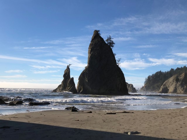 Jagged rock spire jets out of the ocean with hole-in-the-wall rock formation in the background. Ruby Beach, WA