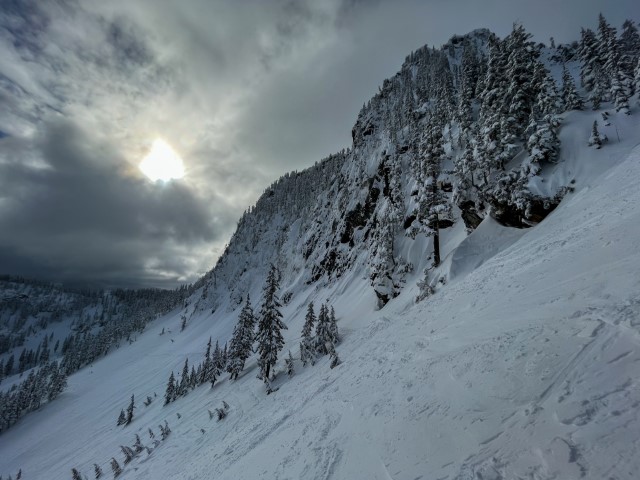 Towering cliff-face coated in snow looms over during a cloudy day.  Snowqualmie Pass, WA